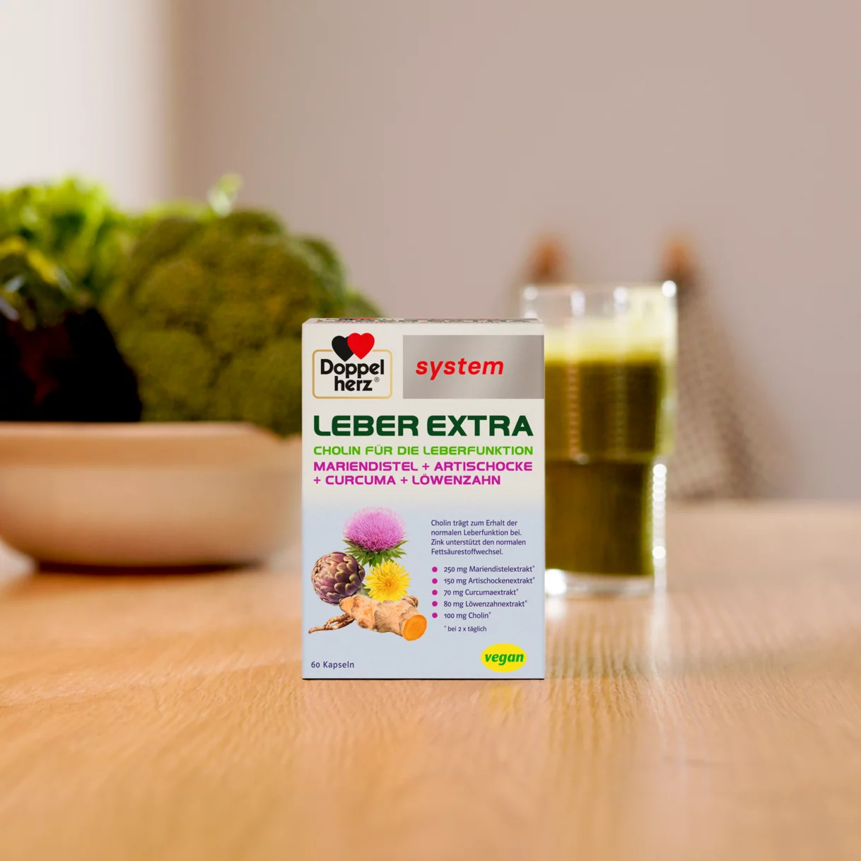 Doppelherz system Leber Extra auf Tisch mit grünem Smoothie und Gemüse im Hintergrund